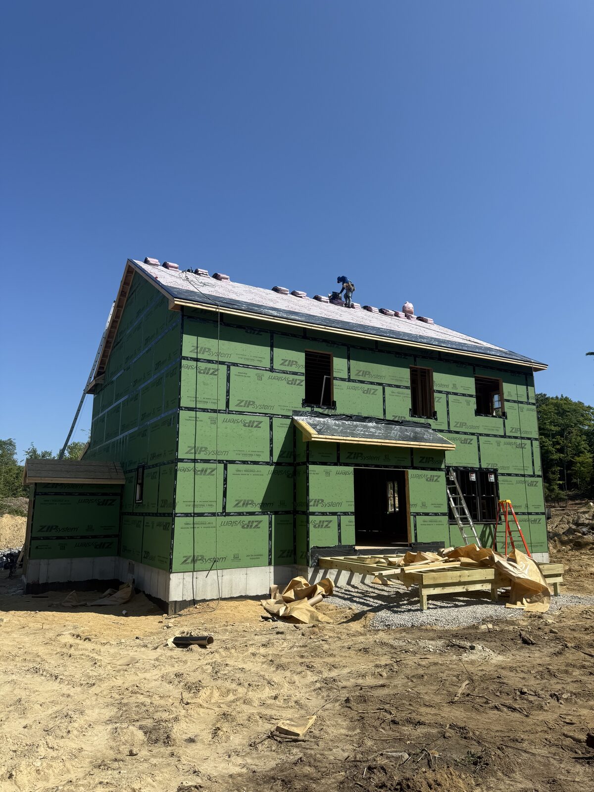 Roofer laying underlayment and starter shingles on a new construction house still wrapped in green sheathing panels